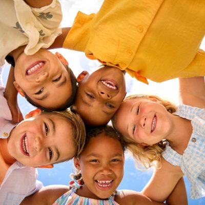 Group Of Multi-Cultural Children Friends Linking Arms Looking Down Into Camera